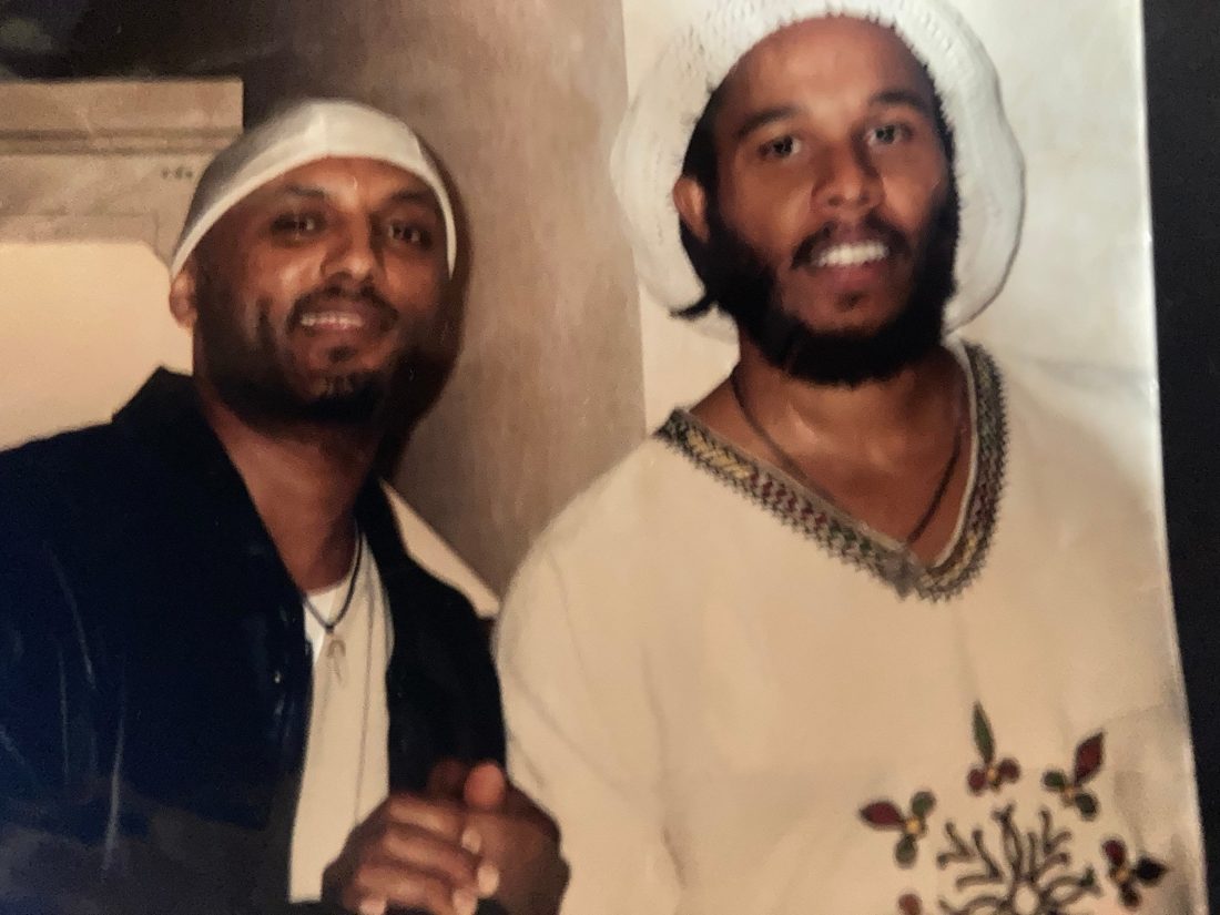 Paolos TK in a white headwrap beside Ziggy Marley in a white knit cap